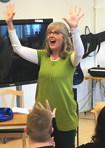 Dr. Gill Brigg facilitating a group exercise, and holds her hands in the air exubilantly